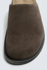 Zueco cerrado de hombre, color verde militar, fabricado en piel con acabado serraje (gamuza). Presenta plantilla acolchada y suela de goma negra con volumen.