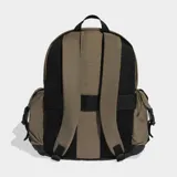 Mochila Adidas de diseño utilitario en color marrón, con compartimento principal amplio, bolsillo frontal con solapa y hebillas ajustables, y bolsillos laterales con solapa. Presenta el logo del trébol en la parte inferior frontal y detalles en negro.