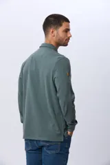 Remera polo de manga larga confeccionada en tejido jersey, con cuello clásico y cierre frontal de tres botones. Presenta un diseño liso con un pequeño logo bordado en el pecho y una etiqueta decorativa en el ruedo.