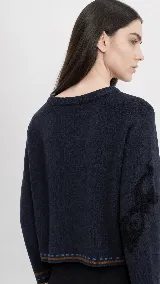 Sweater de lana color azul marino con escote redondo, corte holgado y manga larga. Presenta un bordado decorativo en una de las mangas y detalles de rayas y puntos en contraste en el ruedo y los puños.