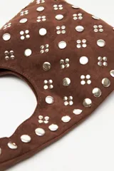 Cartera tipo hobo confeccionada en gamuza negra, con asa integrada y decorada en toda su superficie con tachas metálicas plateadas dispuestas en patrones geométricos.