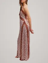 Vestido largo con estampado de ondas en tonos rosa y marrón, con detalles de encaje marrón en el escote y aberturas laterales, tirantes finos y tajo profundo en la pierna.
