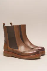 Bota tipo Chelsea de cuero vacuno color suela, con diseño brogue en la puntera y laterales. Presenta paneles elásticos laterales en color marrón oscuro, tirador trasero y suela de goma con plataforma.