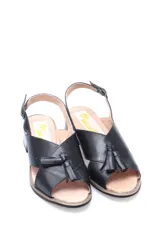 Sandalia de cuero negro con tiras cruzadas en el empeine, detalle de flecos decorativos, cierre con hebilla ajustable en el tobillo y taco bajo cuadrado de madera.