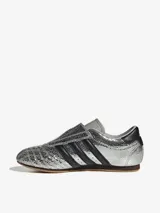 Zapatillas Adidas Taekwondo plateadas con diseño craquelado, inspiradas en el calzado de artes marciales de principios de la década de 2000. Presentan un diseño sin cordones, con las tres tiras clásicas en negro y suela de goma color caramelo.