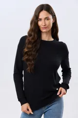 Buzo tejido liso de manga larga, confeccionado en algodón de cuello redondo. Presenta puños, cuello y cintura en punto elástico acanalado, con un pequeño aplique metálico decorativo en el borde inferior.