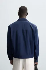 Cazadora bomber azul marino de corte regular fit, confeccionada en tejido de algodón. Presenta cuello solapa, manga larga con puño ajustable de botón, bolsillos de vivo en la cadera, bolsillo interior y bajo con elástico. Cierre frontal con cremallera.