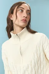 Sweater de tejido de punto con estructura de ochos en color natural, de cuello alto y manga larga. Presenta un bordado de sol en la espalda y puños con franjas de colores en rojo, celeste y amarillo.