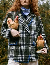 Blazer sastrero de corte oversize, con cuello solapa, manga larga y cierre frontal con botones. Presenta un diseño a cuadros en tonos bordó y blanco, con detalles de costuras bordadas en hilo amarillo en los bolsillos y el ruedo. Incluye forro interior de satén.