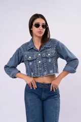 Campera de jean cropped con tachas plateadas distribuidas en el frente, hombros y mangas. Presenta un diseño con bordes deshilachados, cuello clásico y cierre frontal con botones metálicos.