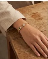 Pulsera rígida de acero con baño dorado, de diseño mallado, con tres dijes circulares incrustados con detalles en ónix, nácar y circonias.