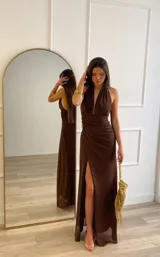 Vestido largo color marrón, con escote profundo en V, cuello halter y falda con tajo lateral. Presenta un diseño drapeado en la cintura.