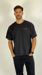 Remera de algodón color gris oscuro con cuello redondo, mangas cortas y estampa pequeña en el pecho con texto y símbolos.