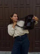 Cartera de hombro confeccionada en cuero y gamuza con diseño de damero, combinando paneles de texturas lisas y aterciopeladas. Presenta una manija trenzada y detalles de costuras artesanales en los laterales.