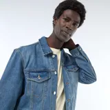 Chaqueta vaquera de corte clásico en color azul, con cierre frontal de botones metálicos, bolsillos frontales con solapa en el pecho y bolsillos ribeteados en los laterales.