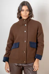 Campera de paño de lana color marrón con diseño oversize. Presenta cuello alto, cierre frontal con botones y detalles en pana azul marino en los puños y en las tapas de los bolsillos frontales.