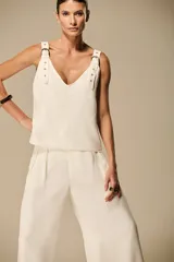 Musculosa color marfil de silueta recta y fluida, con escote en V y tirantes anchos decorados con hebillas metálicas doradas y tachas.