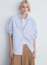 Camisa celeste a rayas verticales blancas, de corte recto, manga larga con puños abotonados, cuello camisero y bolsillo de parche en el pecho.