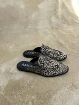 Mocasines destalonados tipo sueco, confeccionados en cuero con estampado animal print tipo dálmata en tonos blanco y negro, con detalle de estribo metálico plateado en el empeine.