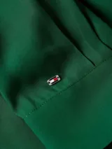 Camisa verde de viscosa con cuello inglés, corte amplio, tapeta oculta, puños abotonados y logo metálico de Tommy Hilfiger en la manga.