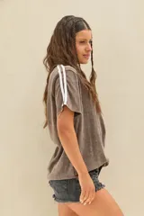 Remera marrón de efecto acid wash con corte oversize, cuello redondo y mangas cortas adornadas con dos líneas blancas paralelas en los laterales.