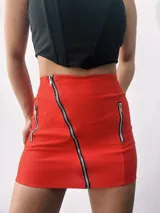Minifalda roja ajustada con cierre diagonal frontal y dos cierres verticales decorativos.