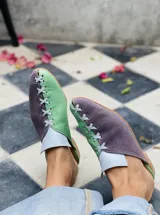 Zapatos tipo mule de punta cerrada y talón abierto, con diseño bicolor en tonos dorado y mostaza, con detalles cruzados en el empeine y suela baja.