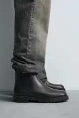 Bota tipo Chelsea fabricada en piel, con diseño de parte superior lisa, piezas elásticas laterales y tirador trasero. Presenta horma redonda y suela con volumen y piso track.