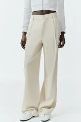 Pantalón gris de tiro alto con bolsillos delanteros y traseros, detalle de pliegues frontales y cierre frontal con cremallera y botón.