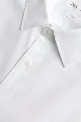 Camisa blanca de corte slim fit, confeccionada en tejido de algodón. Presenta cuello italiano, manga larga con puño abotonado y cierre frontal de botonadura.