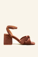Sandalia de gamuza color beige con taco cuadrado, tira ajustable con hebilla en el tobillo y detalle de nudo en la tira delantera.