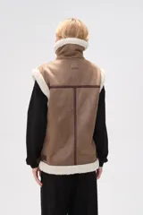 Chaleco negro de efecto cuero con forro y cuello de corderito. Presenta cierre frontal de cremallera, bolsillos laterales y diseño sin mangas.