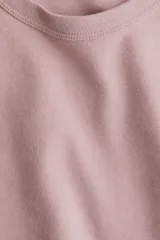 Remera de punto de algodón tupido color rosado, con cuello redondo ribeteado acanalado y mangas cortas.