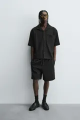 Bermuda de corte relajado color marrón con finas rayas verticales negras. Presenta cintura elástica ajustable con cordón y bolsillos laterales y trasero.