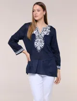 Blusa de corte holgado de inspiración étnica con bordados ornamentales blancos a contraste. Presenta escote en V pronunciado con pechera bordada con motivos arabescos y florales, mangas largas y aberturas laterales en el ruedo.