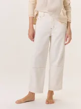 Pantalón de pana color blanco crudo, con textura acanalada vertical (tipo gabardina o pana fina). Es de tiro alto, corte ancho y largo cropped, con costuras visibles en tono contrastante (naranja/tostado) y parches de refuerzo a la altura de las rodillas.