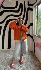 Campera de algodón premium color anaranjado, con cierre frontal, cuello alto, puños y dobladillo en amarillo. Tiene un bolsillo tipo canguro y el logo "K." bordado en el pecho.