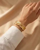 Pulsera tipo esclava rígida de acero con baño de oro, diseñada con una textura detallada que simula una pluma envolvente.