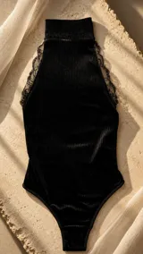 Body negro confeccionado en terciopelo acanalado, con cuello alto, diseño sin mangas y detalles de encaje a lo largo de las sisas y los hombros.
