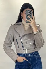 Chaqueta corta tipo biker confeccionada en gamuza color beige, con cierre frontal cruzado, solapas amplias, bolsillos con cierre y cinturón ajustable en la cintura.