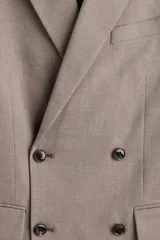 Blazer cruzado de tejido suave color beige/topo, con solapas de pico, ojal decorativo y cierre de doble botonadura. Posee bolsillo superior insertado, dos bolsillos delanteros ribeteados con solapa y botones decorativos en los puños.