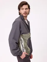 Rompevientos Rusty con cierre frontal, capucha y diseño de bloques de color en gris y verde militar. Cuenta con puños elásticos y logo de la marca en el pecho.