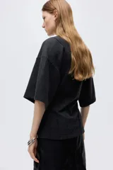Top de punto fino color gris oscuro, con cuello redondo, costuras decorativas frontales, hombros caídos y mangas al codo. Presenta un corte holgado con bajo levemente acampanado.