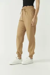 Pantalón de corte holgado confeccionado en mezcla de algodón y lino, color tostado. Presenta cintura elástica con cordón ajustable y puños elásticos en los tobillos.