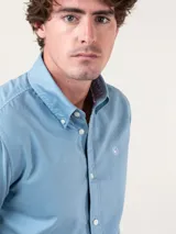 Camisa lisa de hombre color celeste, confeccionada en algodón con acabado vintage, corte regular fit, cuello button-down, cierre frontal de botones y logo bordado en el pecho.