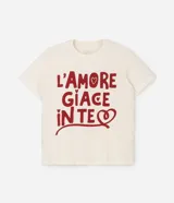 Remera de algodón de corte holgado y largo, con cuello redondo y mangas cortas. Presenta una estampa frontal con la frase 'L'AMORE GIACE IN TE' en color rojo sobre fondo crema.