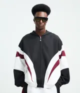 Campera con capucha de estilo deportivo, confeccionada en poliéster con diseño de paneles en colores negro, blanco y bordó. Presenta cierre frontal con cremallera, puños elásticos y bolsillos laterales.