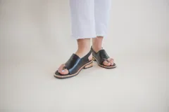 Sandalias de cuero negro con tira entre los dedos, talón descubierto y hebilla lateral.