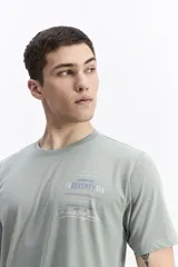 Remera de manga corta color marrón oscuro, con escote redondo y fit regular. Presenta un estampado frontal con texto en color amarillo y blanco.