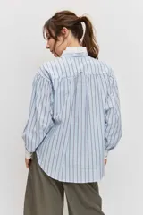 Camisa de rayas celestes y marrones, de corte holgado y manga larga, con cuello en V y detalles blancos en el cuello y los puños.